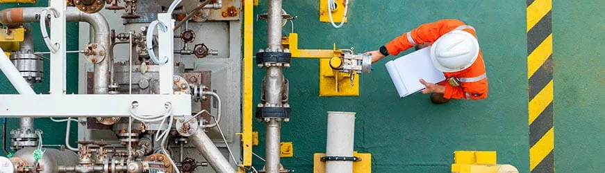 Image prise du dessus, d’un ouvrier actionnant une très grosse machine industrielle. Il porte un équipement orange et un casque de protection.